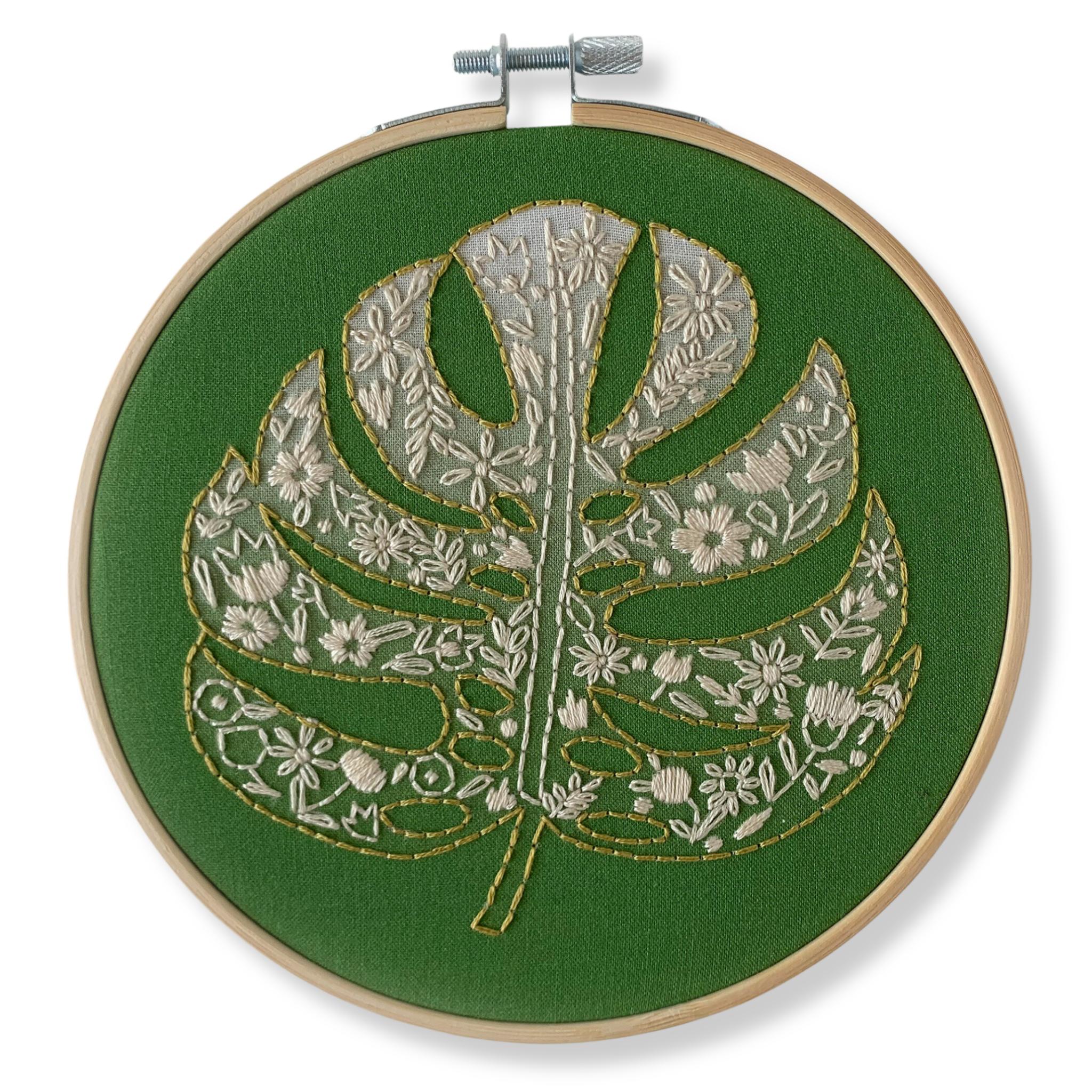 All inclusive embroidery kit for a 6 inch hoop including a monstera palm leaf with floral details on a dark green background by Rikrack