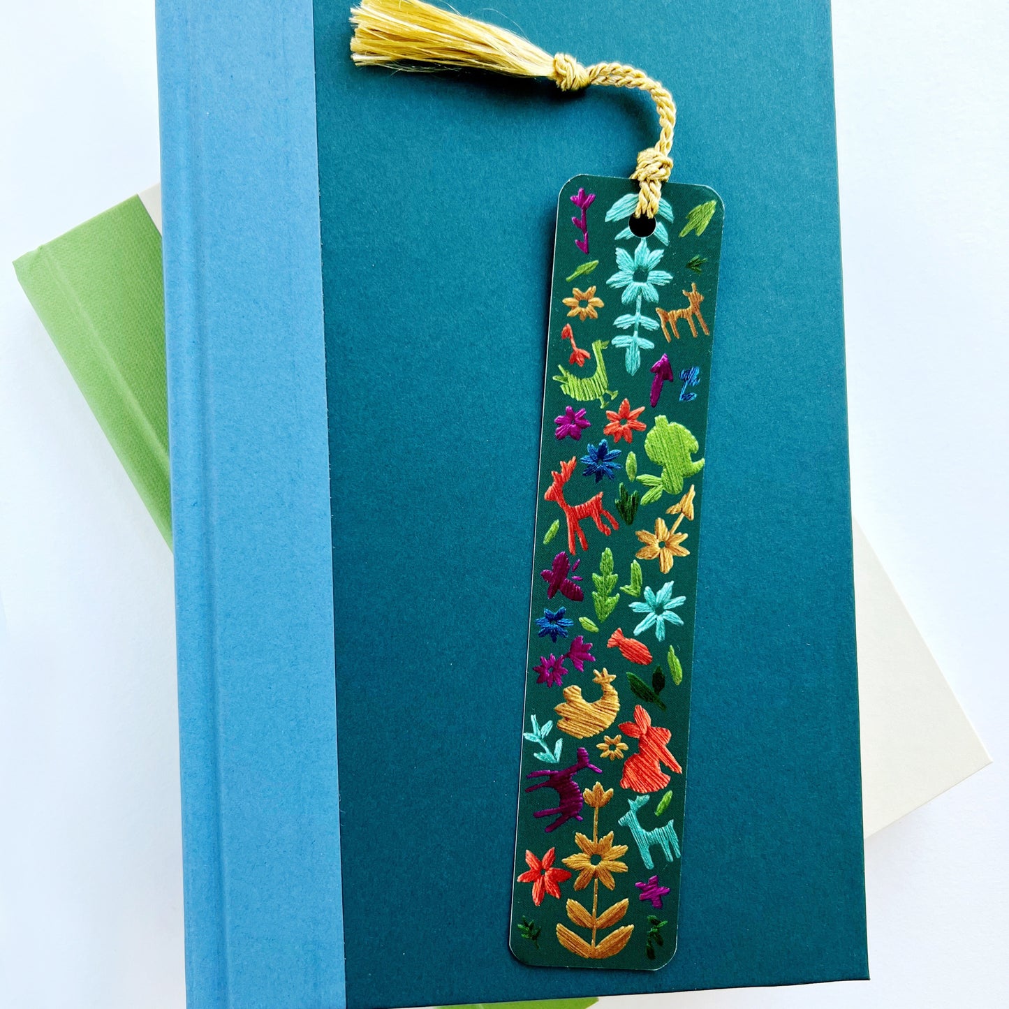 Embroidered bookmark with dark green background and stiches of animals in a forest